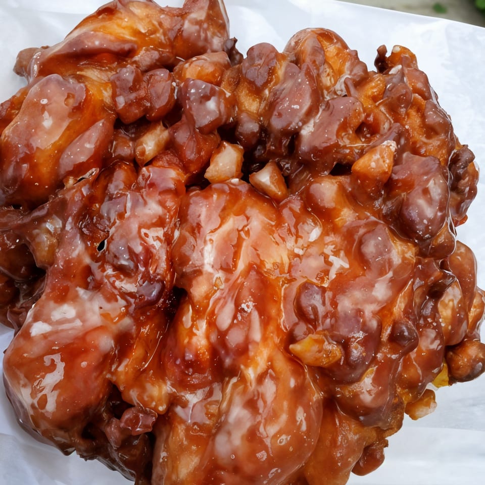 Close-up of a large, glazed apple fritter from KB Donuts and Sandwiches, with a rich brown color.